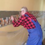 Centrum Integracji Społecznej i pomoc socjalna - na zdjęciu starszy mężczyzna wykonujący prace remontowe, układa mozaikę na ścianie
